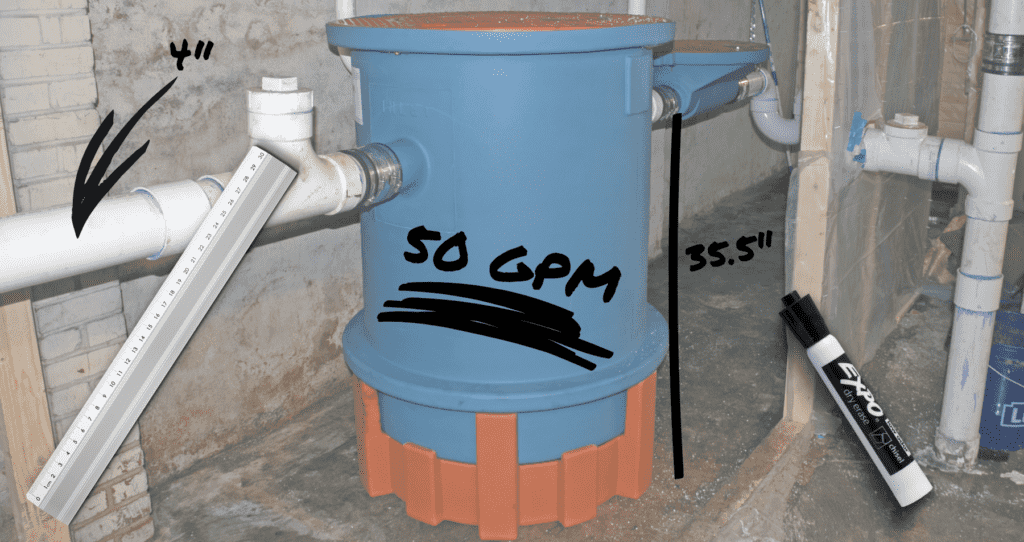 A blue and orange cylindrical Super-capacity grease interceptor tank with pipes on both sides, labeled "50 GPM." A ruler and dry-erase marker show a pipe height of 41 inches and tank height of 35.5 inches in an unfinished setting.