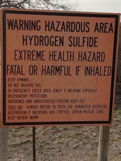 A posted sign near the super-capacity grease interceptor warns of a hazardous area with hydrogen sulfide, stating extreme health hazard; fatal or harmful if inhaled. It provides safety instructions and emergency procedures in case of exposure.